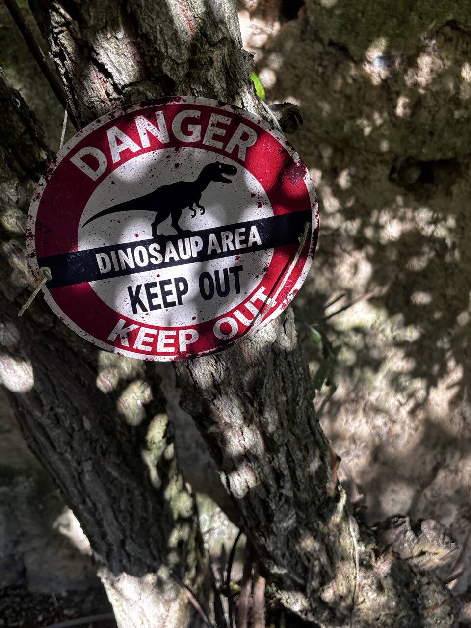 Cartel de Dinosaur Area Danger Keep Out colgado de un árbol
