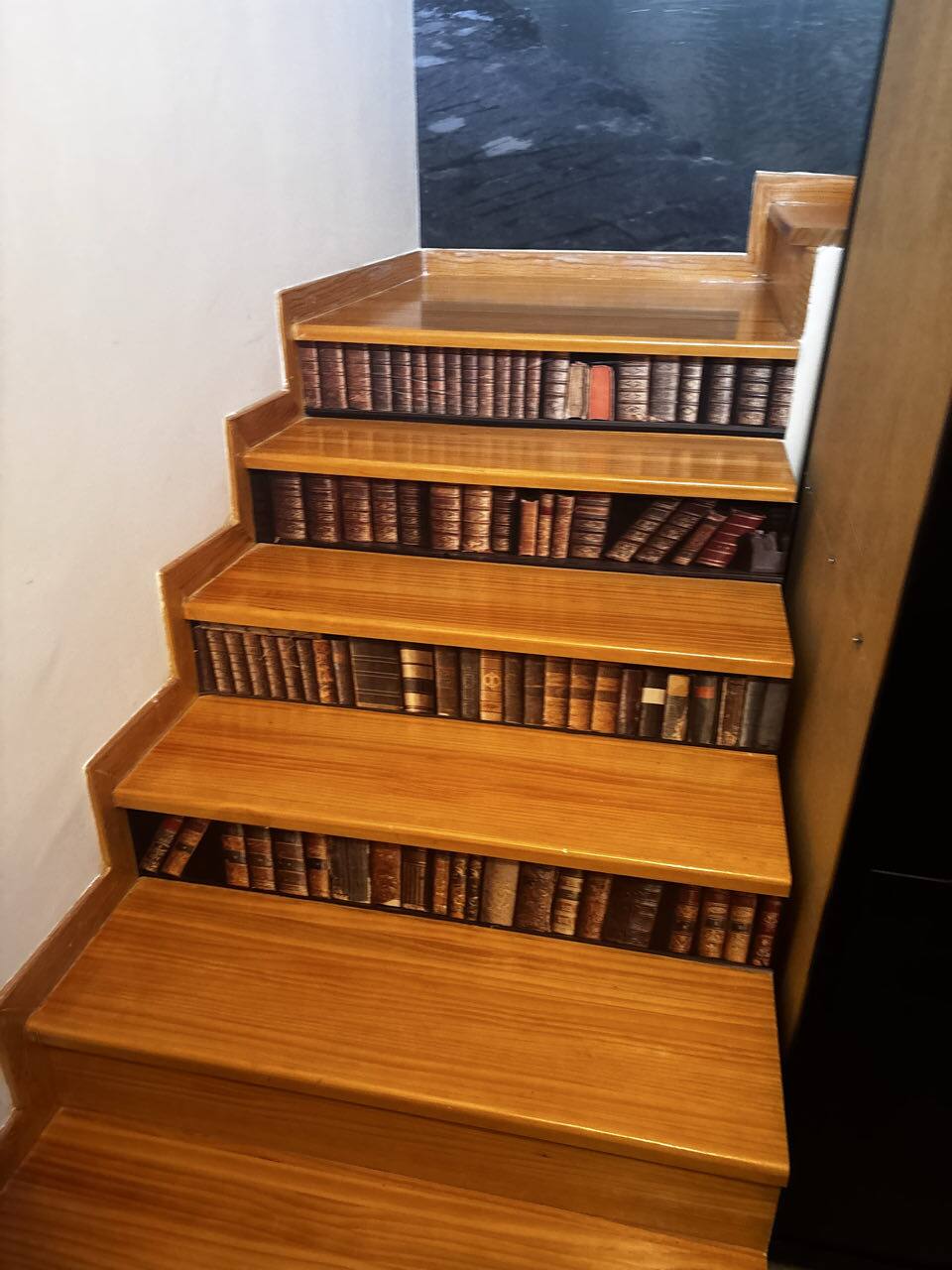 Escalera de madera cuyas contrahuellas imitan una biblioteca